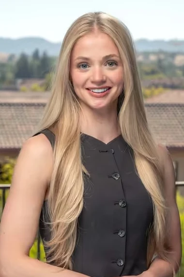 Mary smiling on a balcony, tile rooftops and green hills behind her
